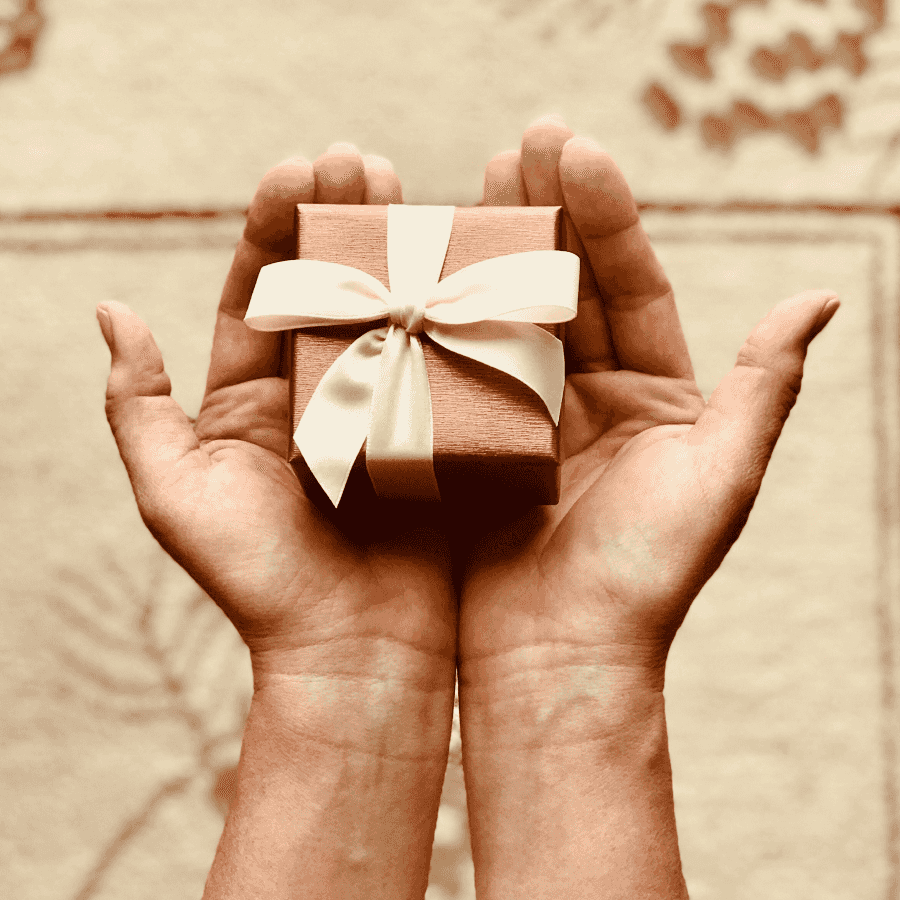 Hands holding a small gift box wrapped in brown paper with a cream ribbon bow, symbolizing a versatile gift card option for any occasion.